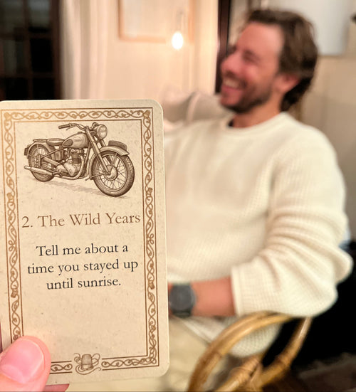 A person holding up a vintage-style card with a motorcycle illustration and the text: 2. The Wild Years. Tell me about a time you stayed up until sunrise.