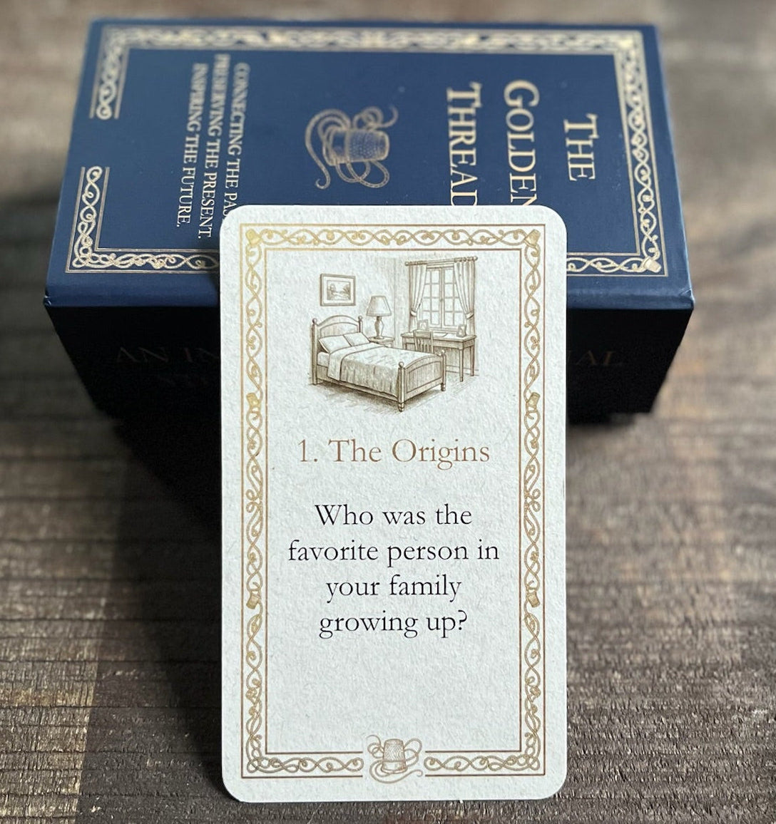 A card with question 'Who was the favourite person in your family growing up?' in category '1. The Origins' from 'The Golden Thread' deck is displayed in front of its dark blue box on a dark wooden tray.