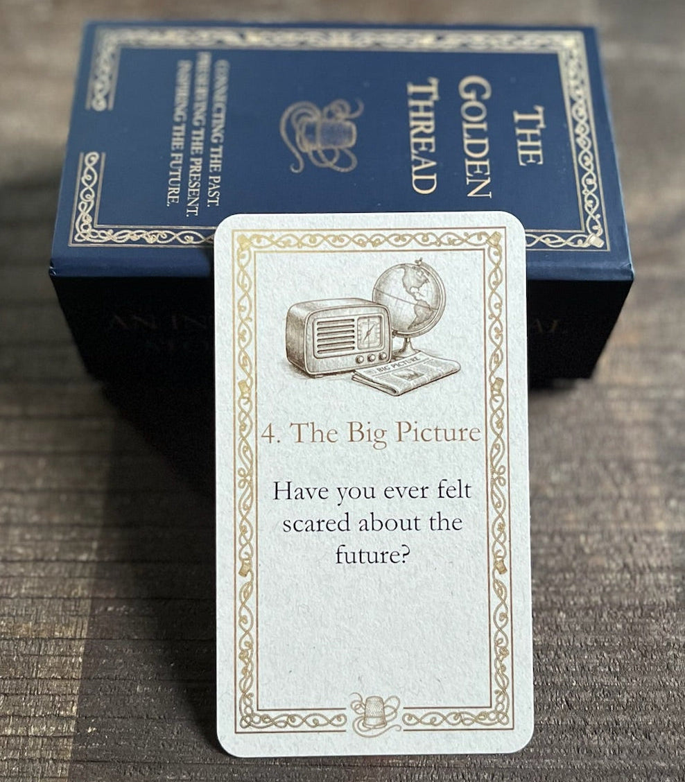 A card with question 'Have you ever felt scared about the future?' in category '4. The Big Picture' from 'The Golden Thread' deck is displayed in front of its dark blue box on a dark wooden tray.