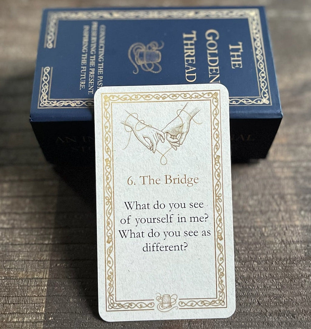 A card with question 'What do you see of yourself in me?' in category '6. The Bridge' from 'The Golden Thread' deck is displayed in front of its dark blue box on a dark wooden tray.