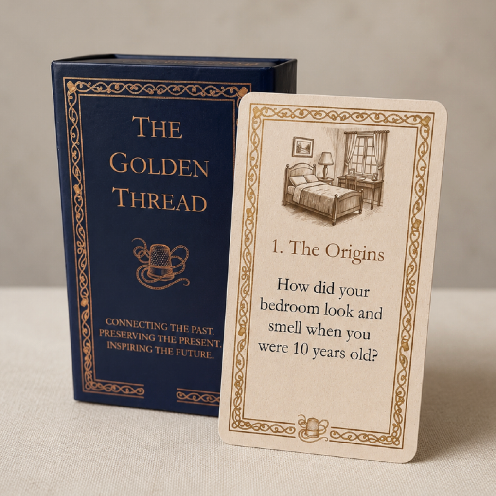 A luxury boxed card deck called The Golden Thread, with a navy blue box and gold etching together with a sample card which is cream coloured featuring gold decorative borders and a vintage bedroom etching sepia illustration. The card text asks about bedroom look and smell when aged 10.