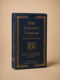 The Golden Thread Card Game Extension Pack box, featuring a dark navy blue cover with ornate gold borders and gold lettering, set against a solid beige background.